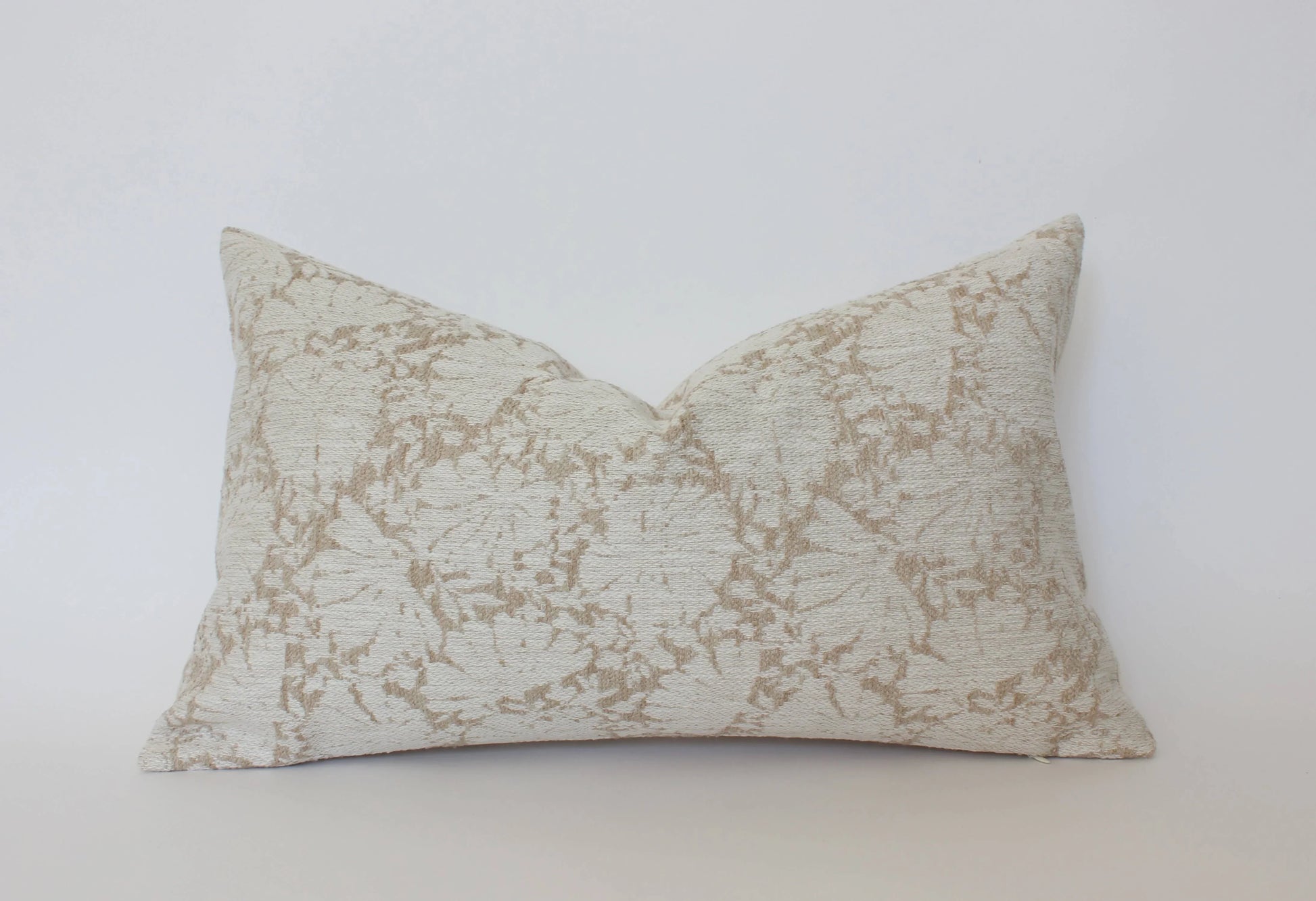 Rectangular beige and cream textured throw pillow with floral pattern on white background. Come see us at Awaken, Franklin, Tennessee