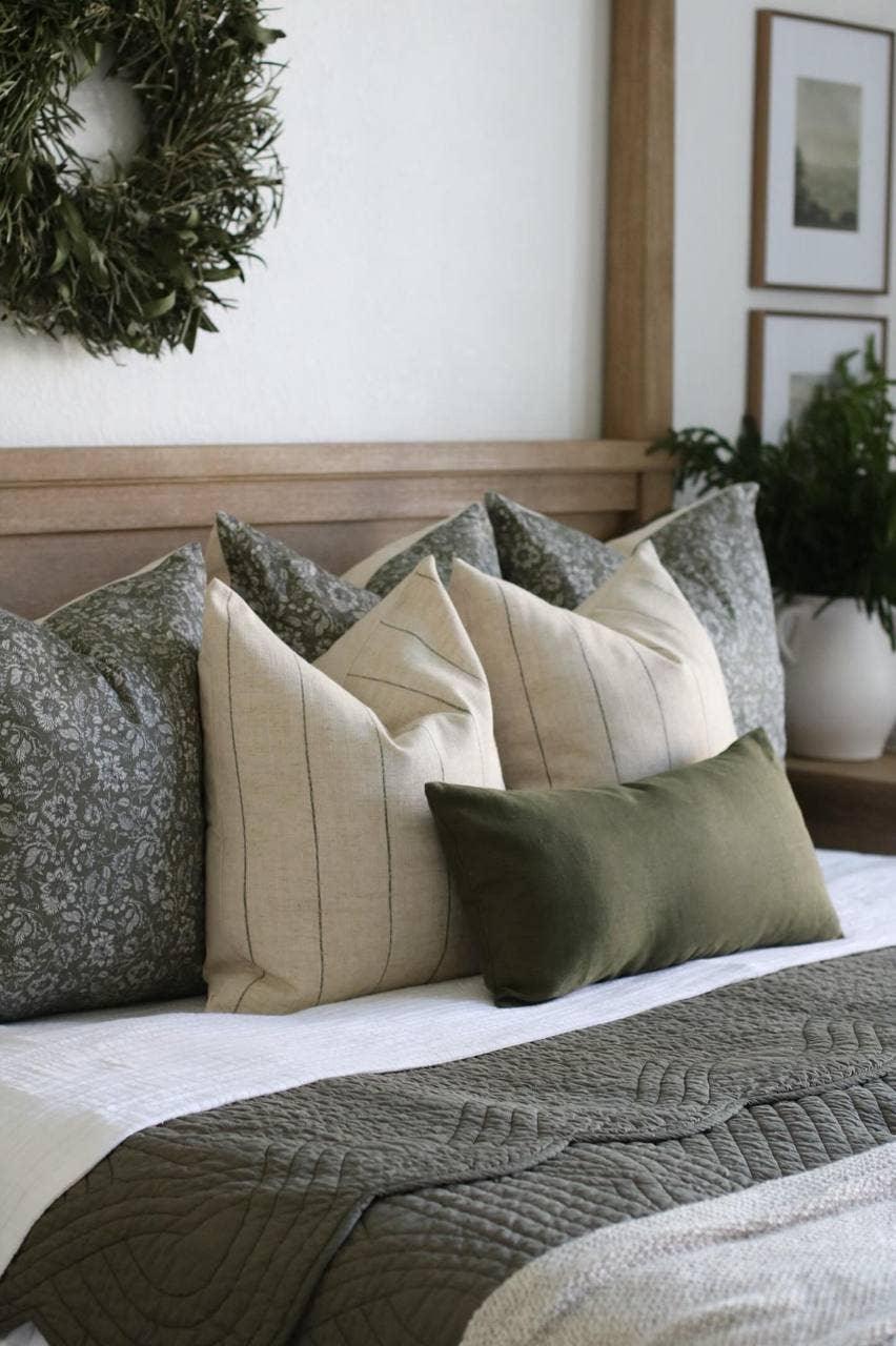 Cozy bed with green floral and beige striped pillows, quilted bedspread, and plant decor. Come see us at Awaken, Franklin, Tennessee