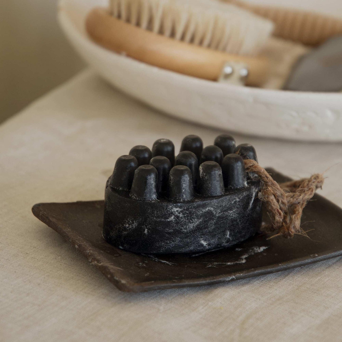 Black exfoliating massage soap bar with wooden handle brush and loofah in a basket. Come see us at Awaken, Franklin, Tennessee