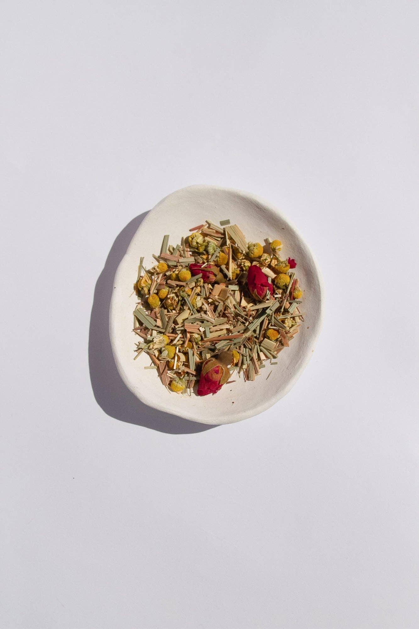 White ceramic bowl with dried chamomile, lemongrass, and rosebuds on white surface. Come see us at Awaken, Franklin, Tennessee