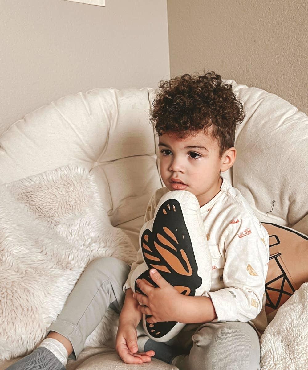 Young child holding butterfly pillow on cozy chair, Come see us at Awaken, Franklin, Tennessee