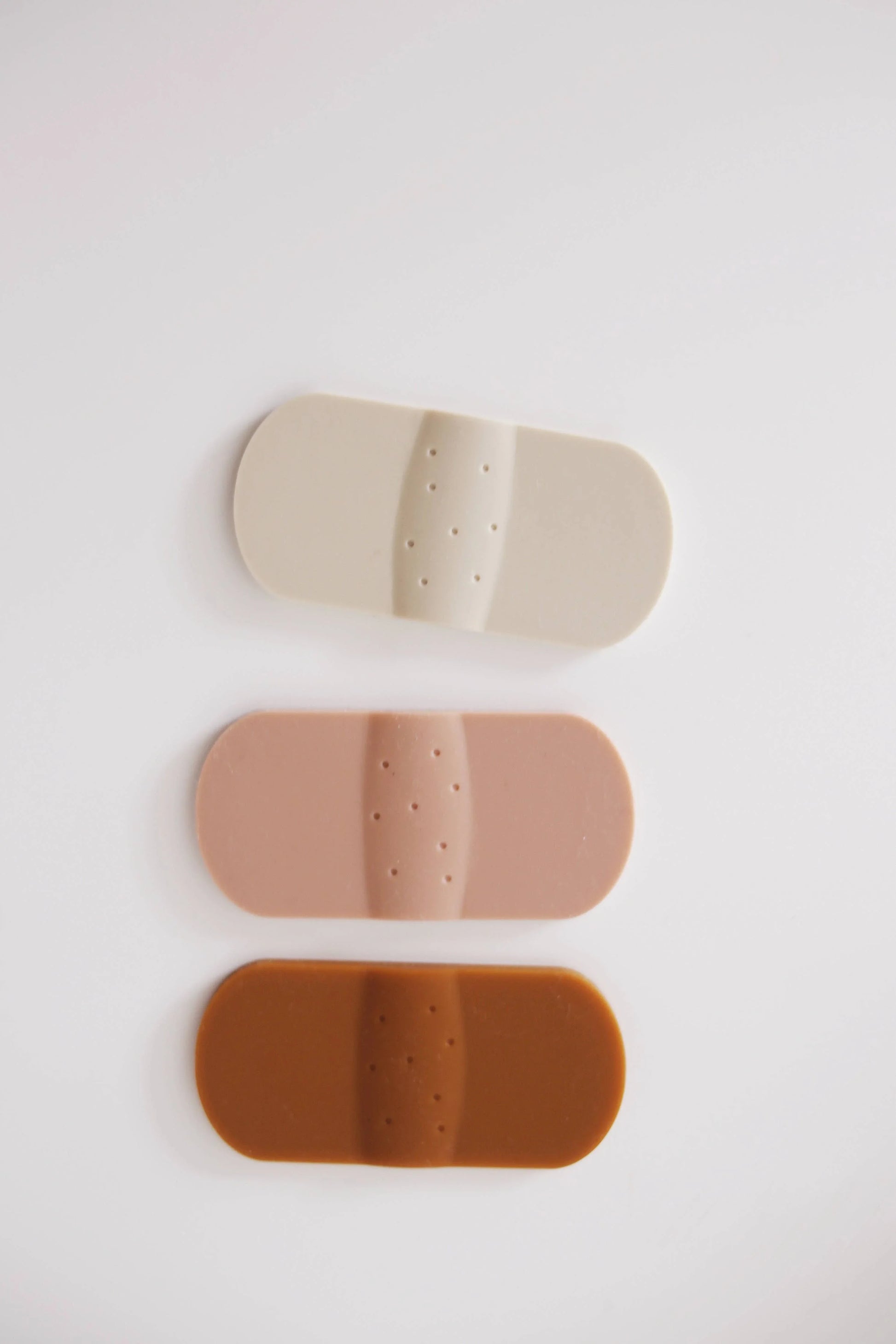 Three adhesive bandages in light beige, medium tan, and dark brown on white background. Come see us at Awaken, Franklin, Tennessee