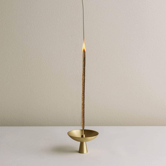 Burning incense stick in a modern gold holder on white surface with beige background. Come see us at Awaken, Franklin, Tennessee