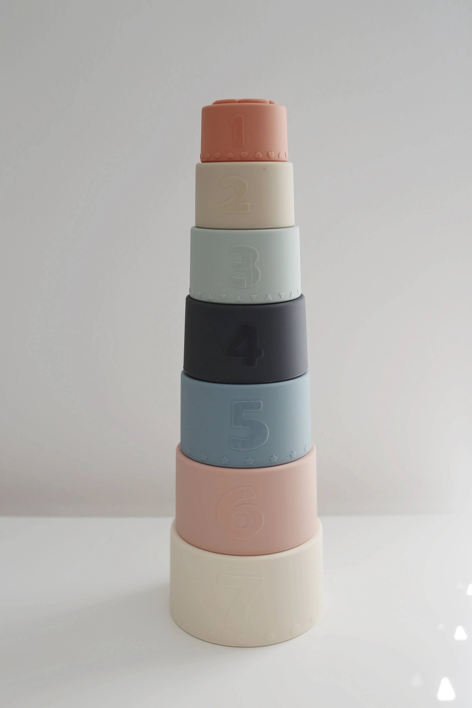 Stacked pastel-colored silicone numbered cups from 1 to 7 on white surface, minimal background. Come see us at Awaken, Franklin, Tennessee