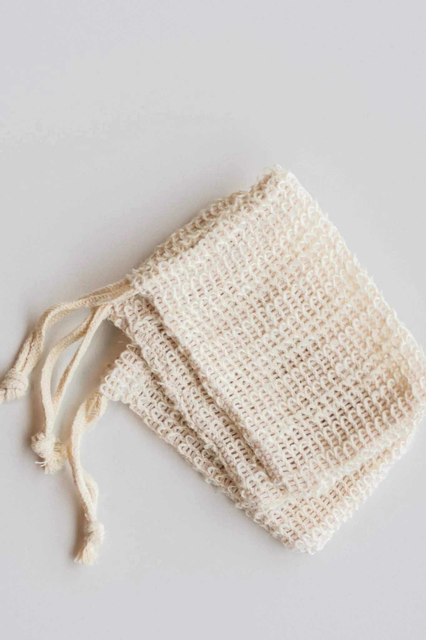 Two natural cotton mesh drawstring bags on white surface, eco-friendly reusable storage. Come see us at Awaken, Franklin, Tennessee