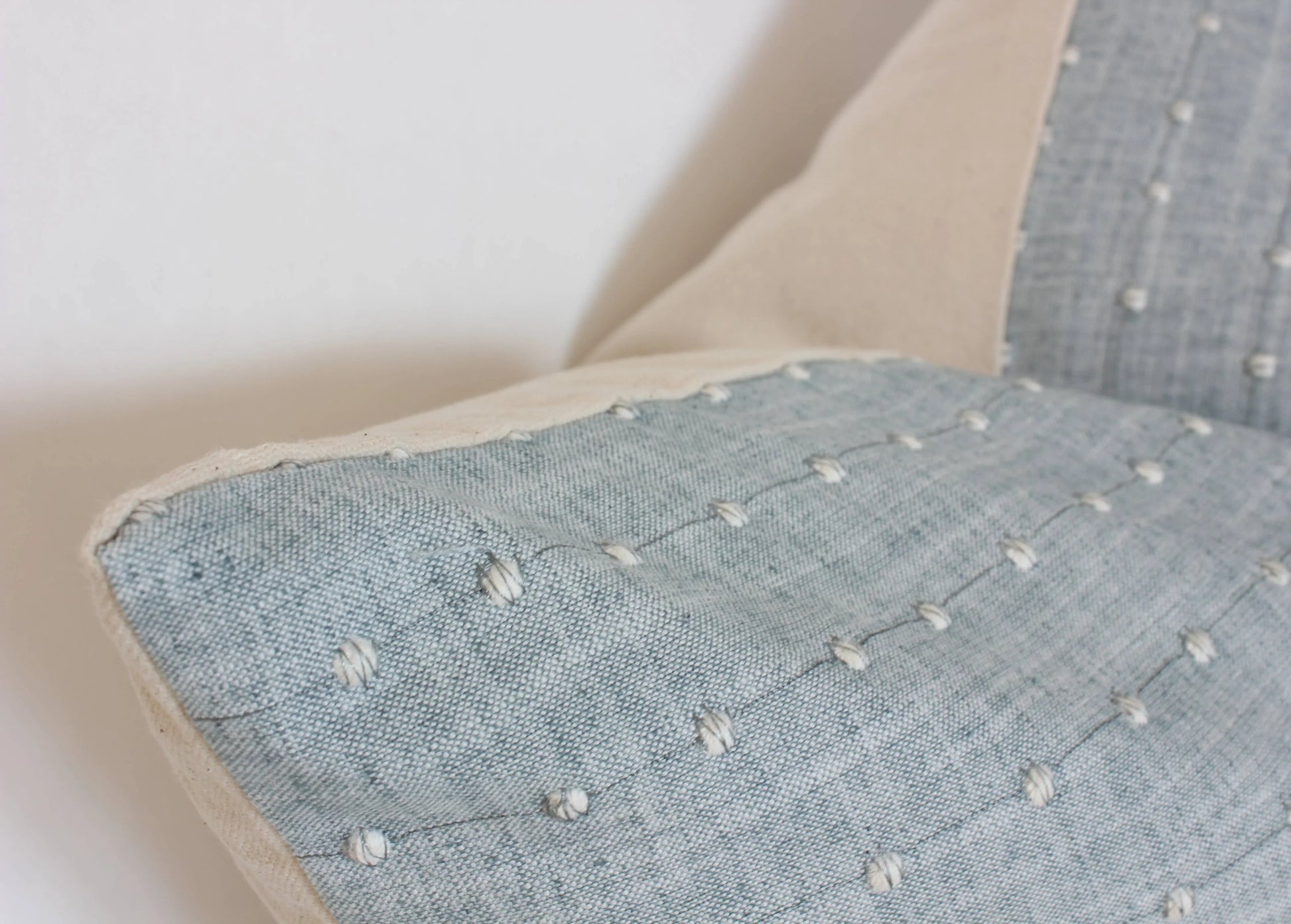 Close-up of a blue textured fabric pillow with white tufted dots on a beige edge. Come see us at Awaken, Franklin, Tennessee
