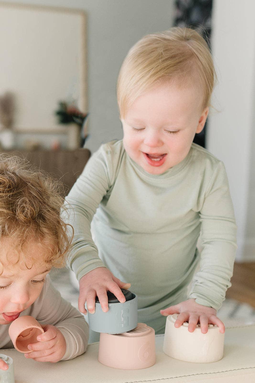 Two toddlers playing with pastel stacking cups indoors, soft natural light. Come see us at Awaken, Franklin, Tennessee
