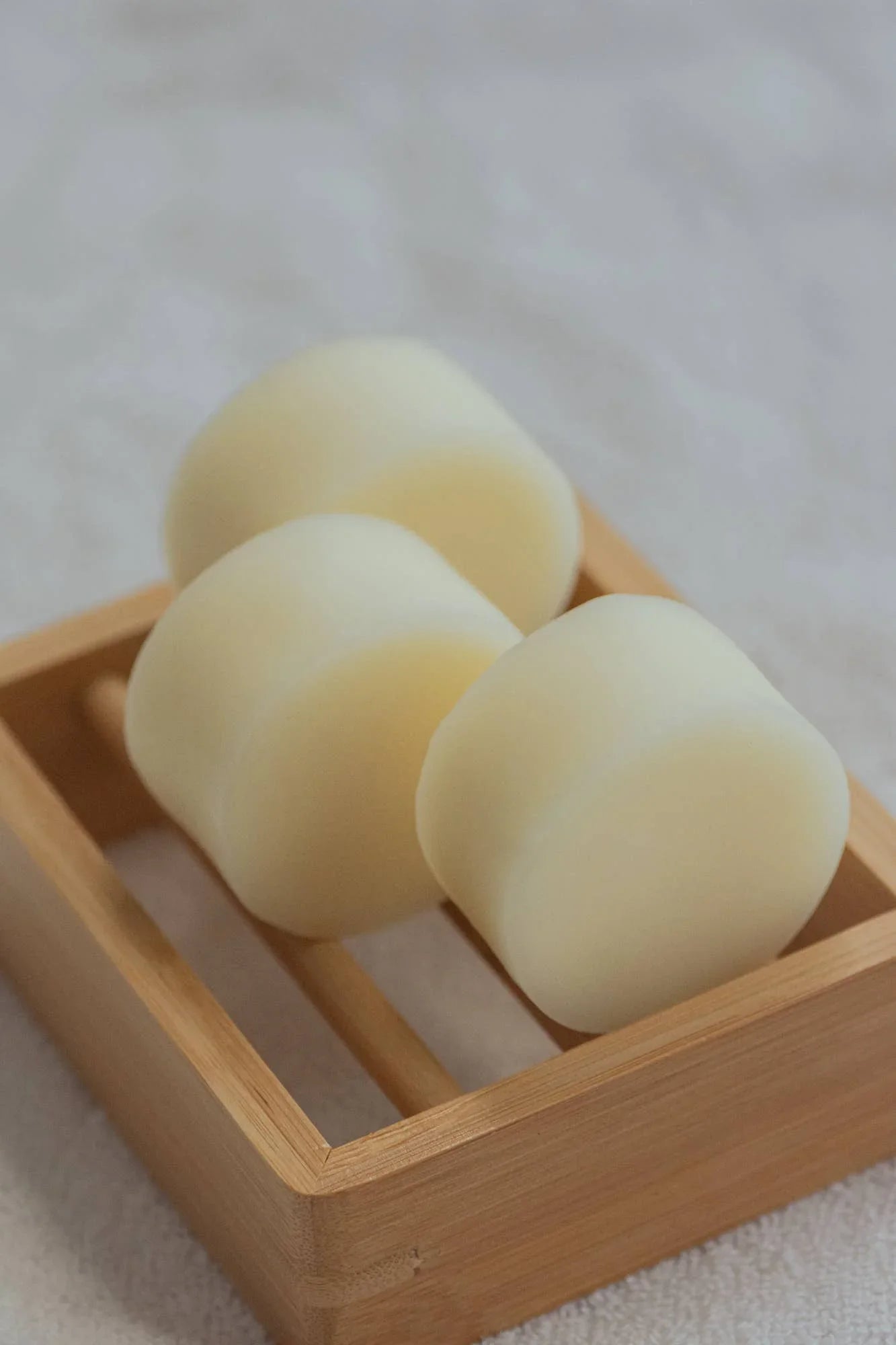 Three smooth white soap bars in a wooden soap dish on a white towel. Come see us at Awaken, Franklin, Tennessee