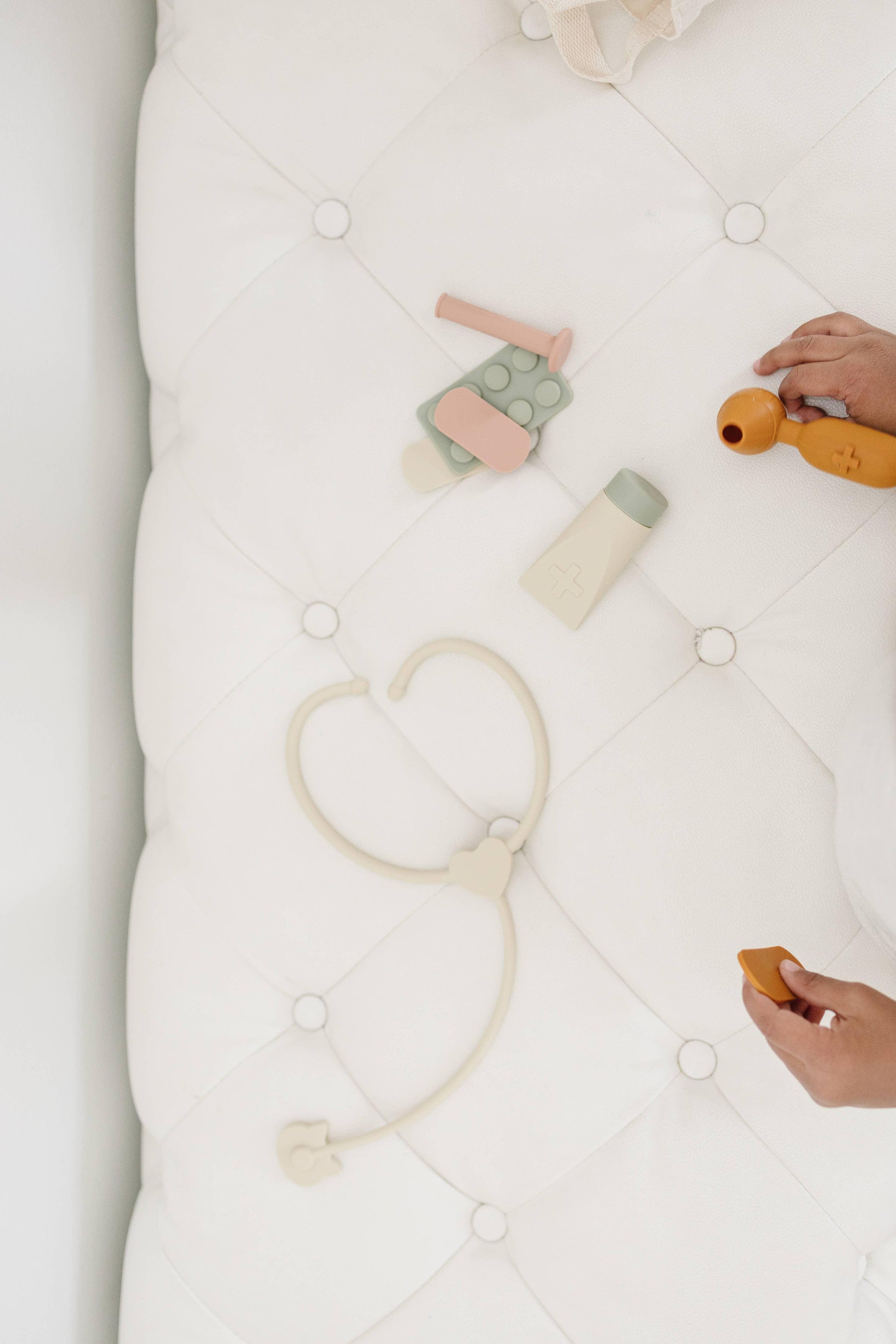Child playing with pastel-colored toy medical kit on white quilted surface. Come see us at Awaken, Franklin, Tennessee