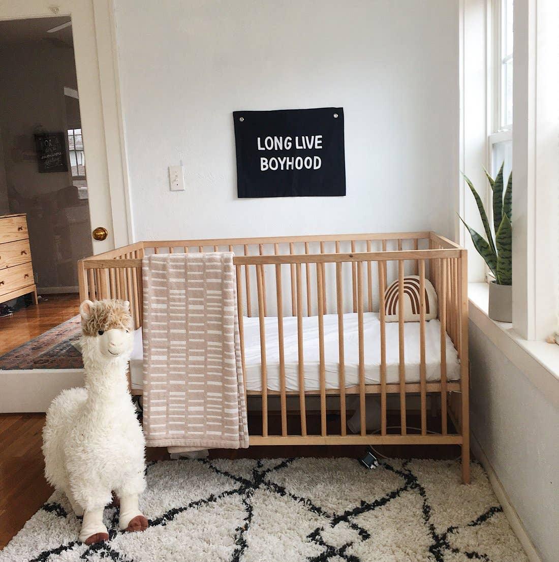 Modern nursery with wooden crib, plush llama, wall sign 'Long Live Boyhood', cozy decor, Come see us at Awaken, Franklin, Tennessee