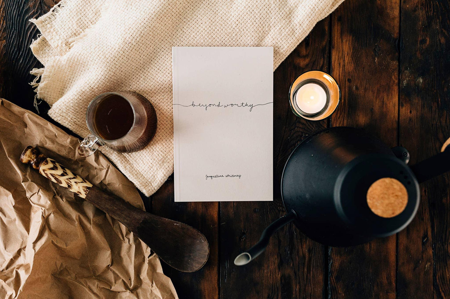 Book titled Beyond Worthy by Jacqueline Whitney on wooden table with coffee, candle, and wooden spatula. Come see us at Awaken, Franklin, Tennessee