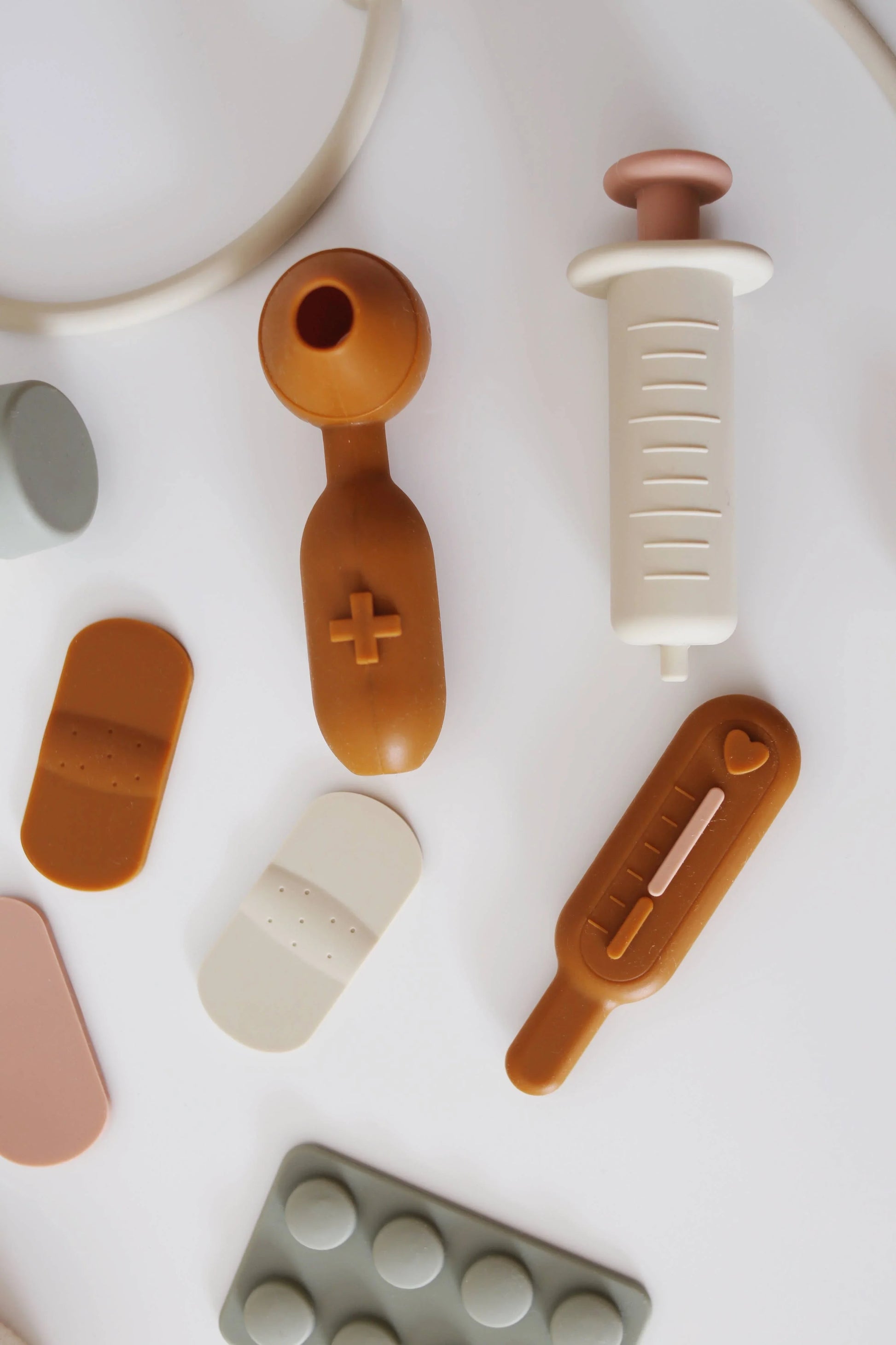 Assorted toy medical items including bandages, syringe, and thermometer on white surface. Come see us at Awaken, Franklin, Tennessee