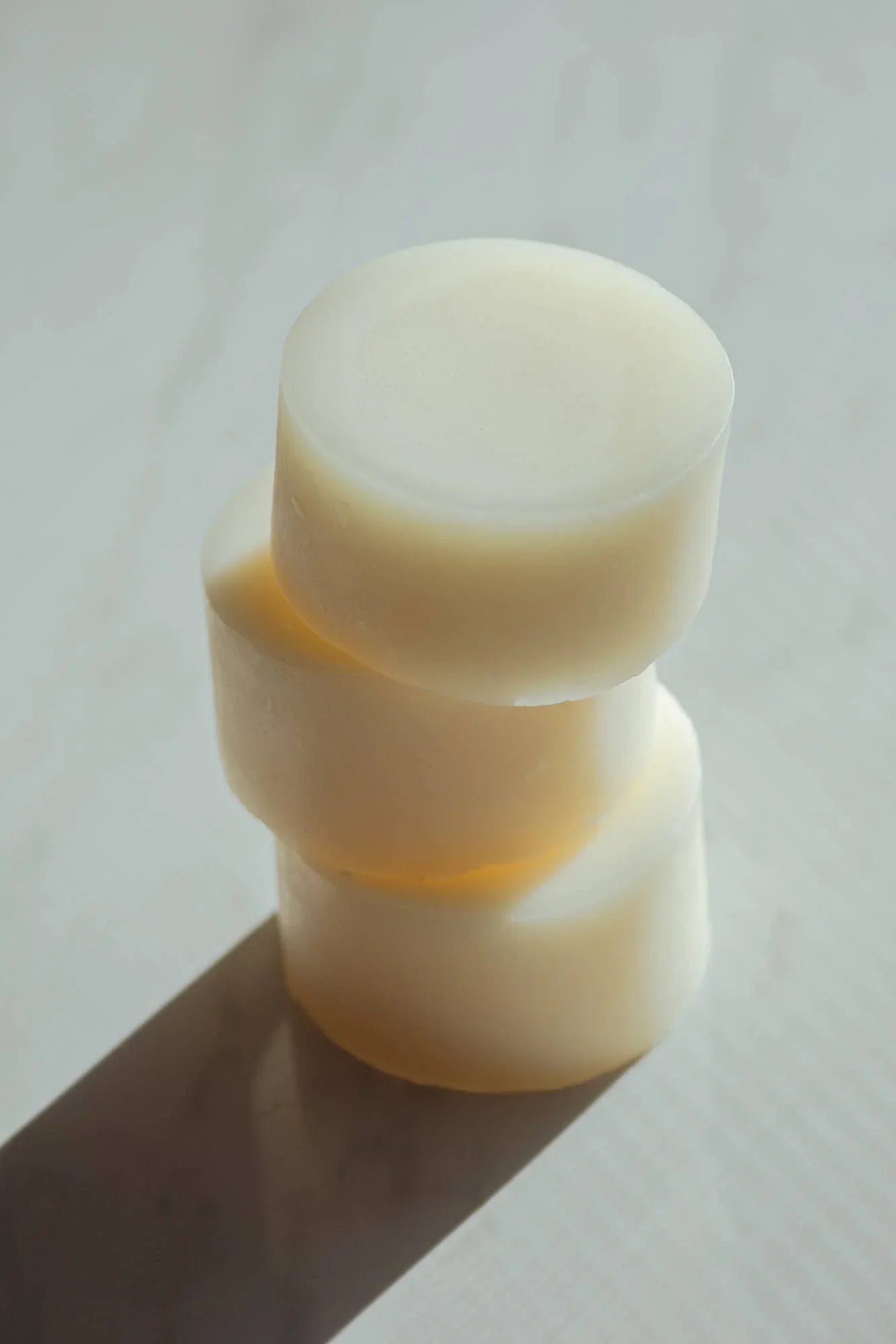 Stack of three round natural soap bars on a white surface with shadows, minimalistic style. Come see us at Awaken, Franklin, Tennessee