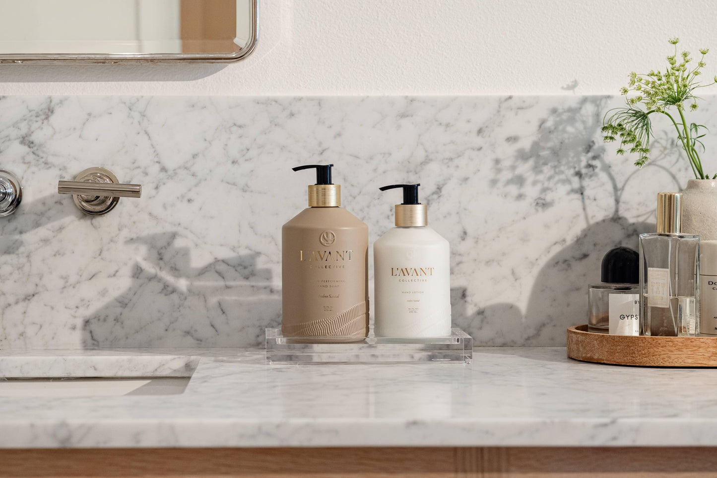 L'Avant Collective hand soap and lotion on marble bathroom counter, greenery and perfumes nearby. Come see us at Awaken, Franklin, Tennessee