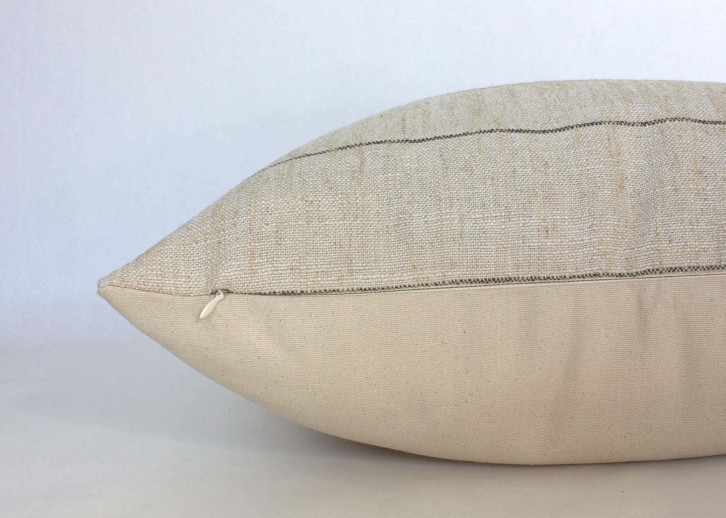 Beige decorative pillow with textured fabric and zipper detail on plain background. Come see us at Awaken, Franklin, Tennessee