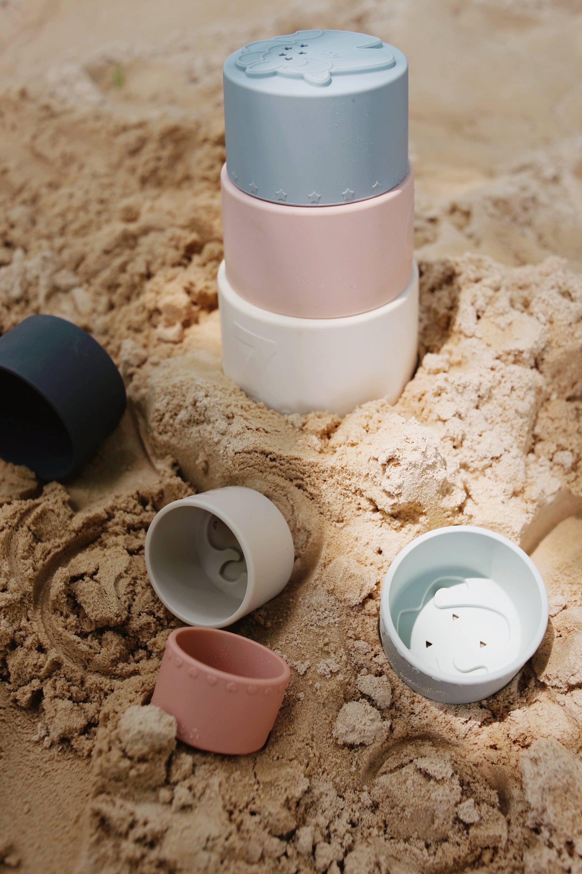 Stacked pastel-colored sand molds and cups on textured beach sand, kids beach toys. Come see us at Awaken, Franklin, Tennessee