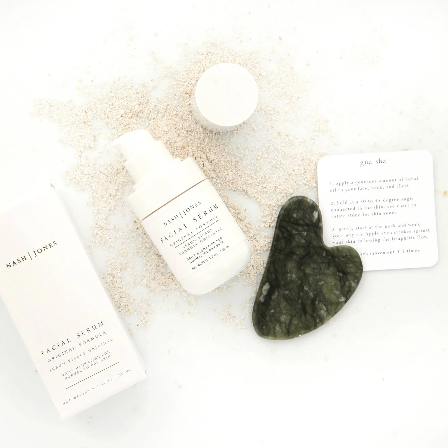 Nash | Jones facial serum with gua sha tool and instructions on white surface sprinkled with powder. Come see us at Awaken, Franklin, Tennessee