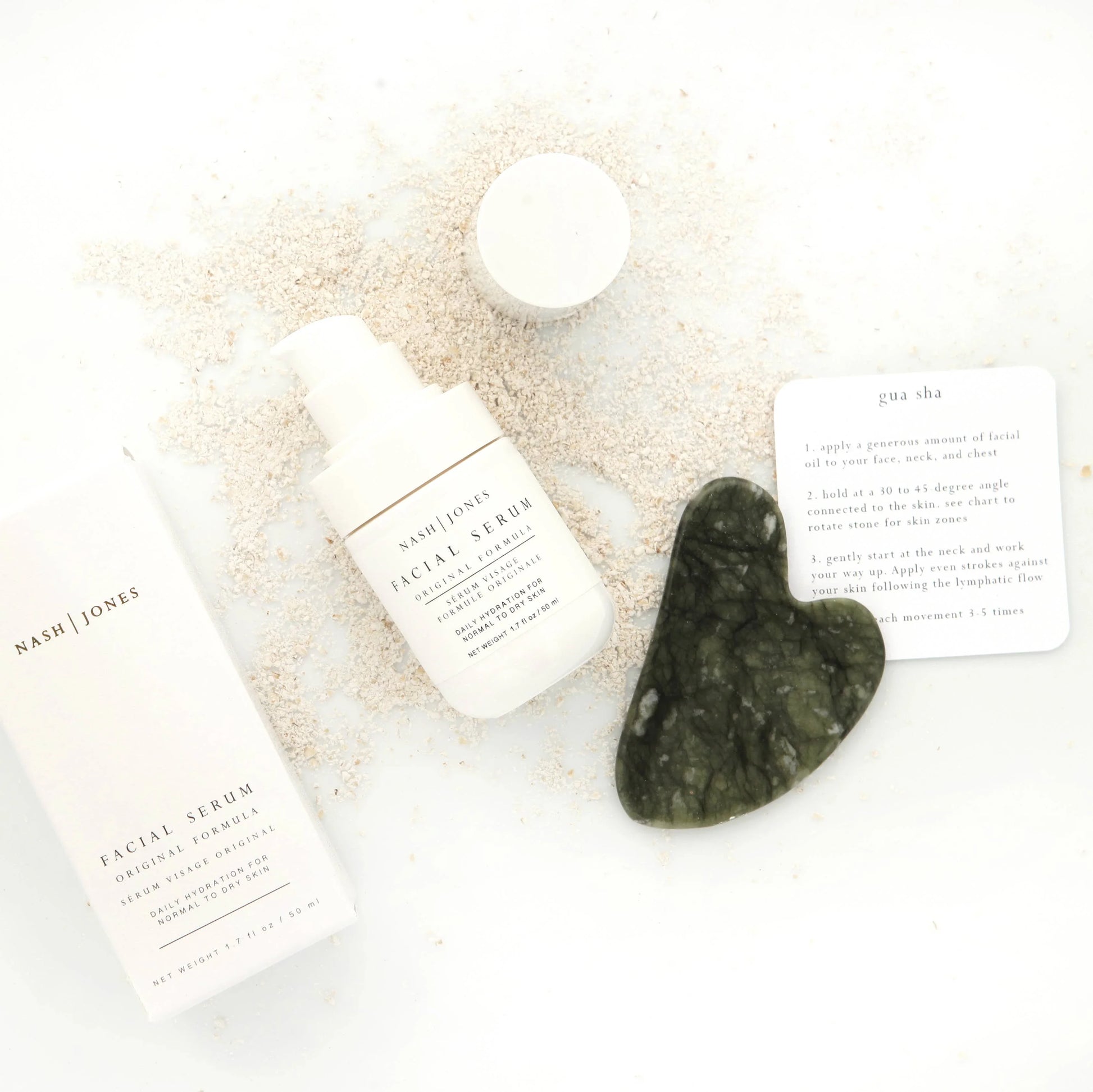 Nash | Jones facial serum with gua sha tool and instructions on white surface sprinkled with powder. Come see us at Awaken, Franklin, Tennessee
