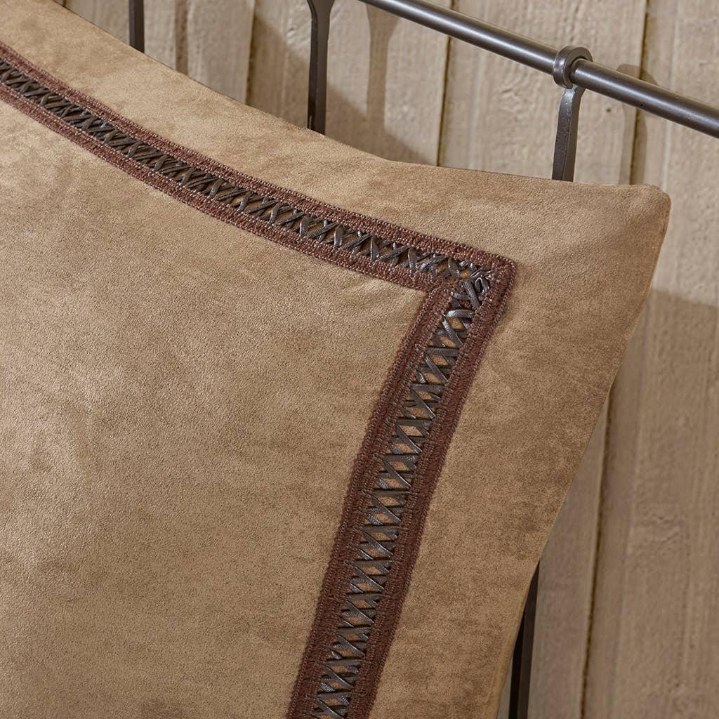 Brown suede pillow with leather lace trim on metal bed frame against wood wall. Come see us at Awaken, Franklin, Tennessee