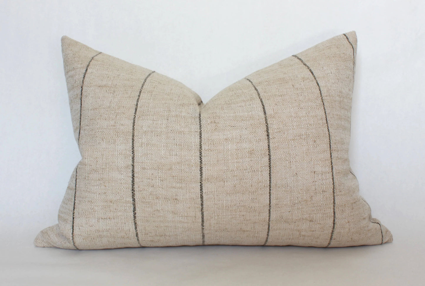 Beige lumbar pillow with thin black vertical stripes on white background. Come see us at Awaken, Franklin, Tennessee
