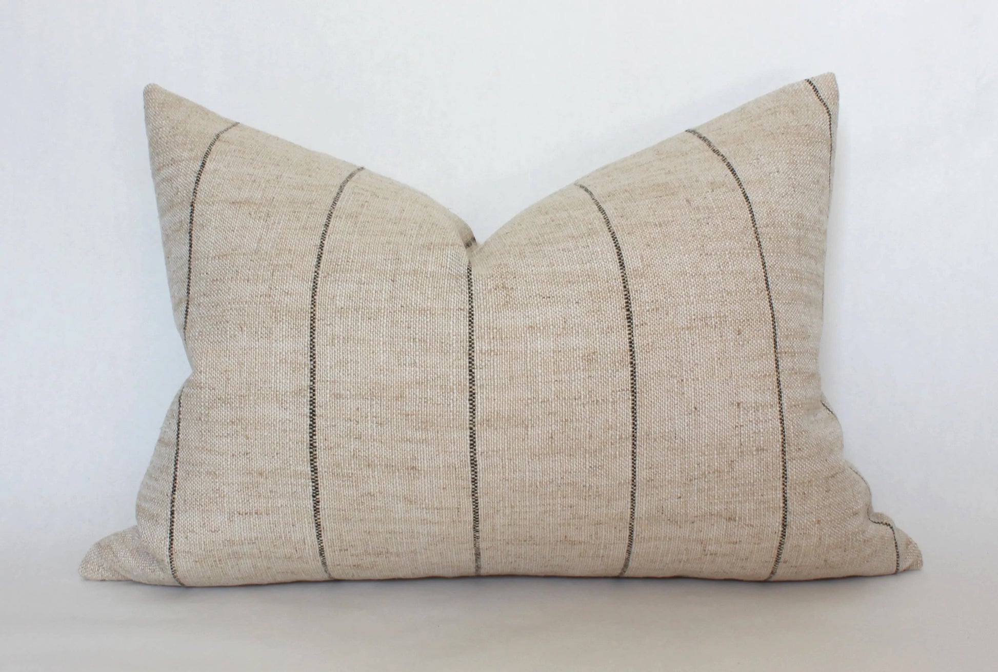 Beige lumbar pillow with thin black vertical stripes on white background. Come see us at Awaken, Franklin, Tennessee