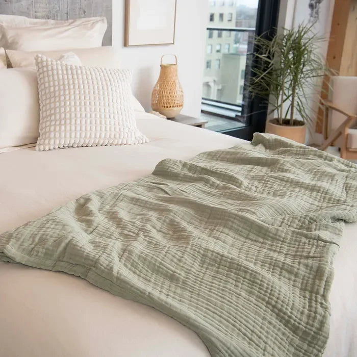 Light green muslin adult blanket on modern bed with decorative pillow, cozy bedroom decor. Come see us at Awaken, Franklin, Tennessee.