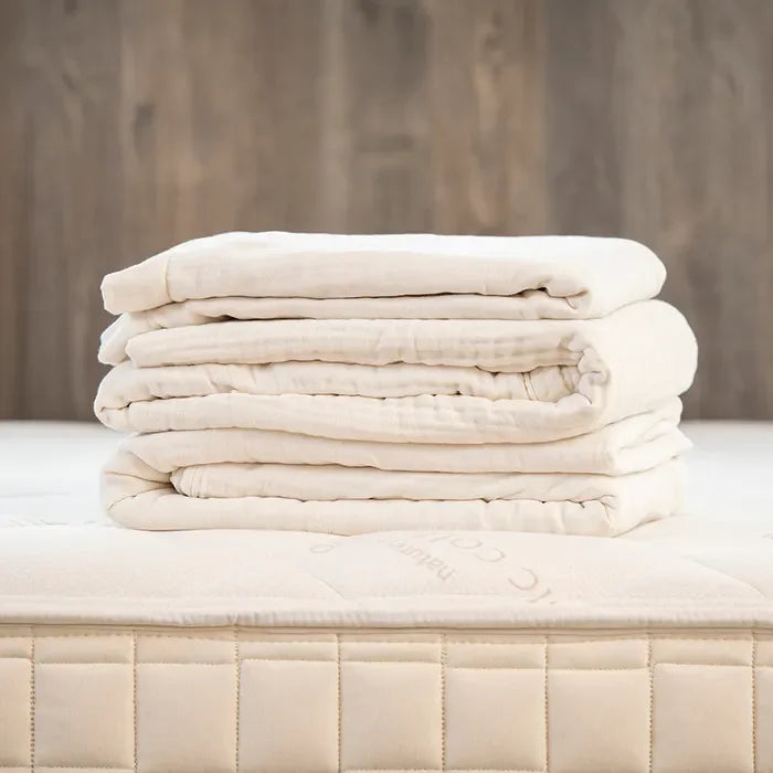 Folded cream muslin adult blanket on bed, neutral decor. Come see us at Awaken, Franklin, Tennessee.