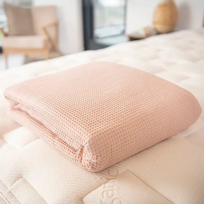 Folded pink waffle blanket on a cream bed, cozy bedding. Come see us at Awaken, Franklin, Tennessee.