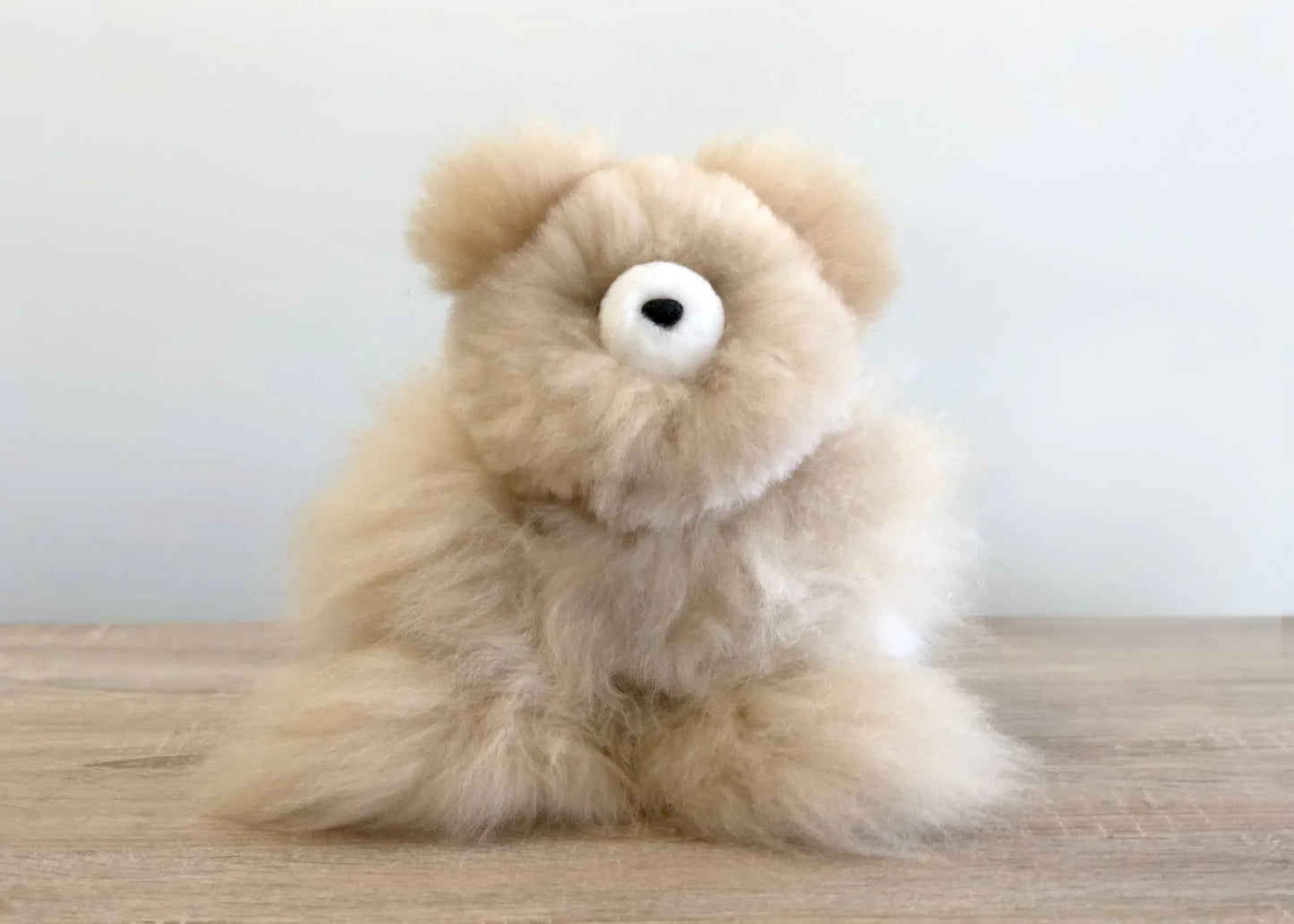 Fluffy beige teddy bear plush on wooden surface with plain light background. Come see us at Awaken, Franklin, Tennessee