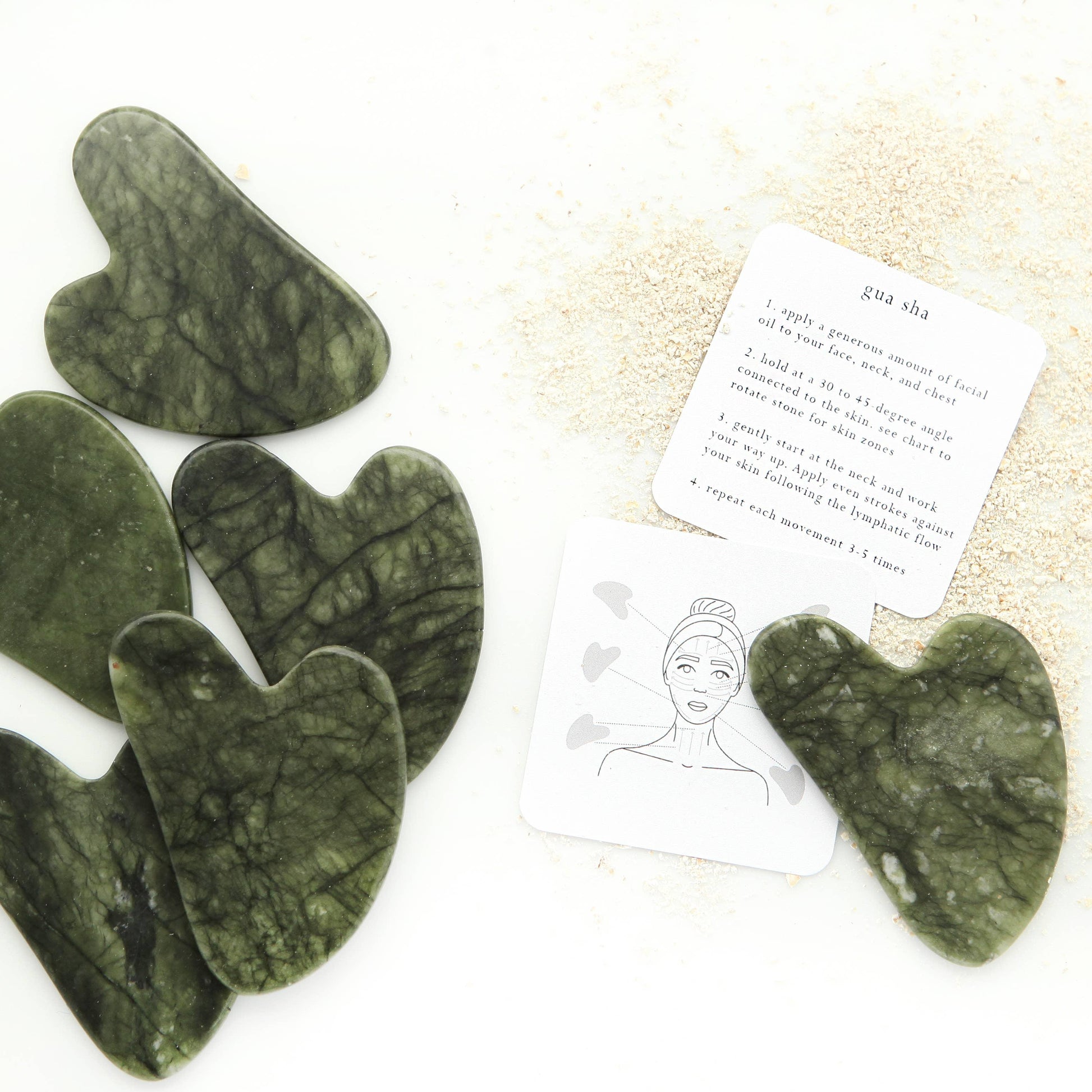 Green jade gua sha facial massage tools with instruction cards on white background come see us at Awaken, Franklin, Tennessee
