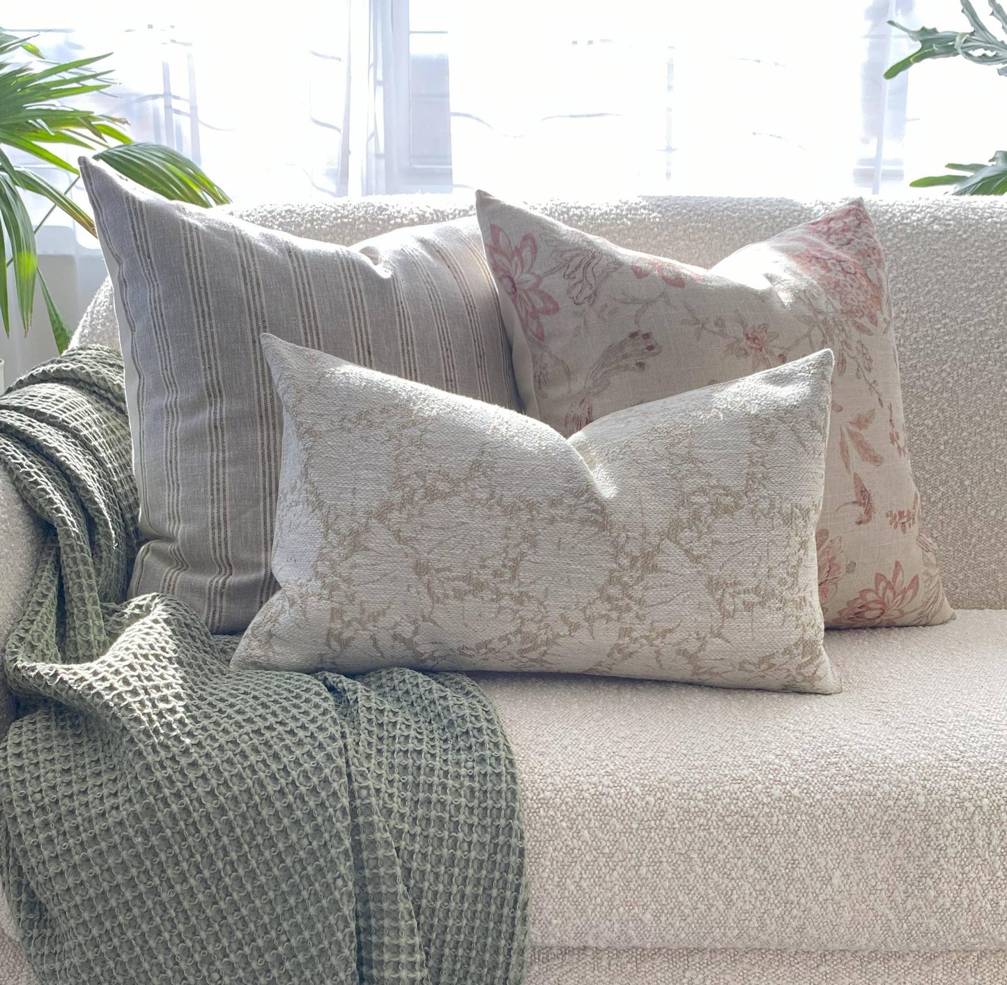 Cozy couch with three decorative pillows and a green knitted throw blanket in bright room. Come see us at Awaken, Franklin, Tennessee