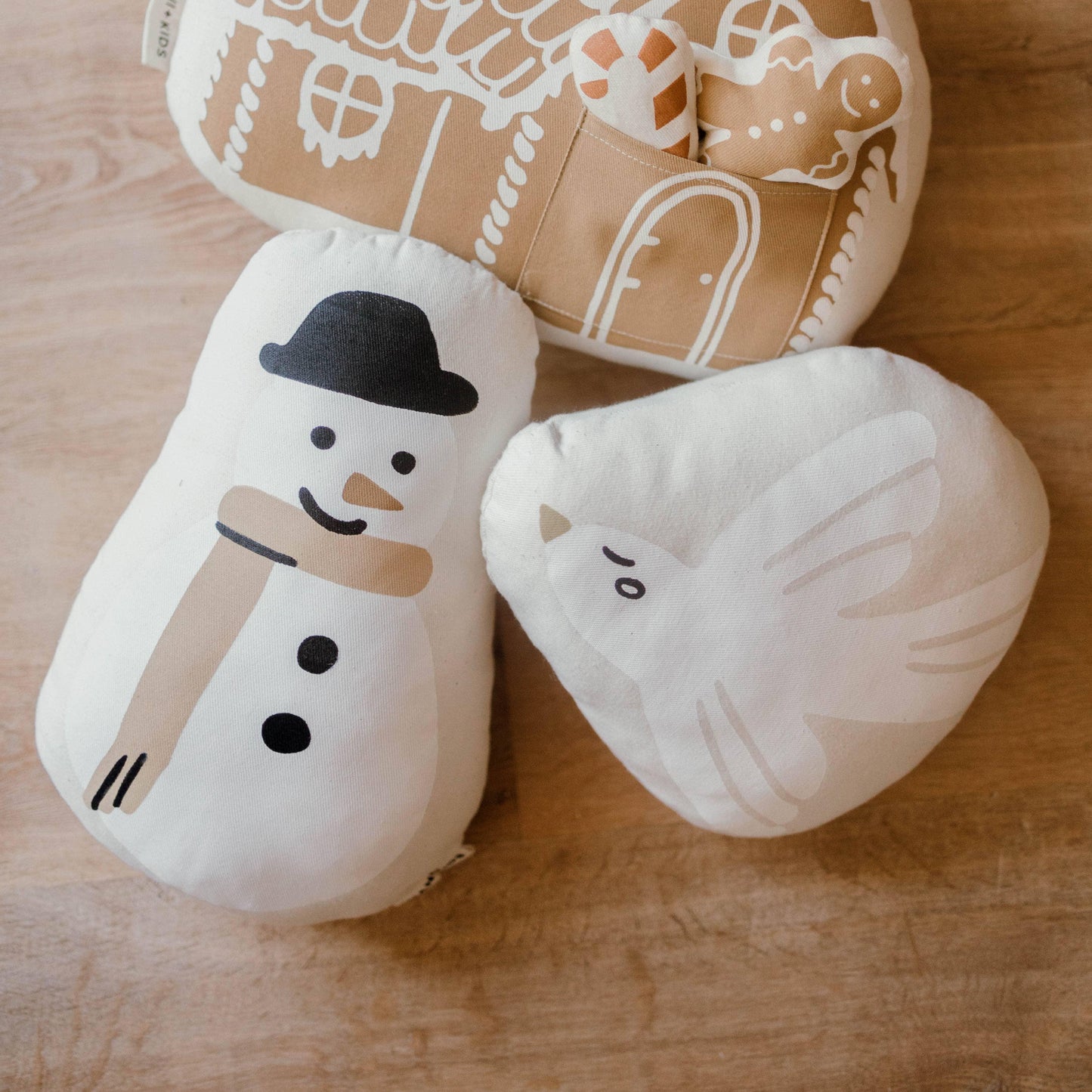 Snowman, dove, and gingerbread plush pillows on wood. Come see us at Awaken, Franklin, Tennessee.