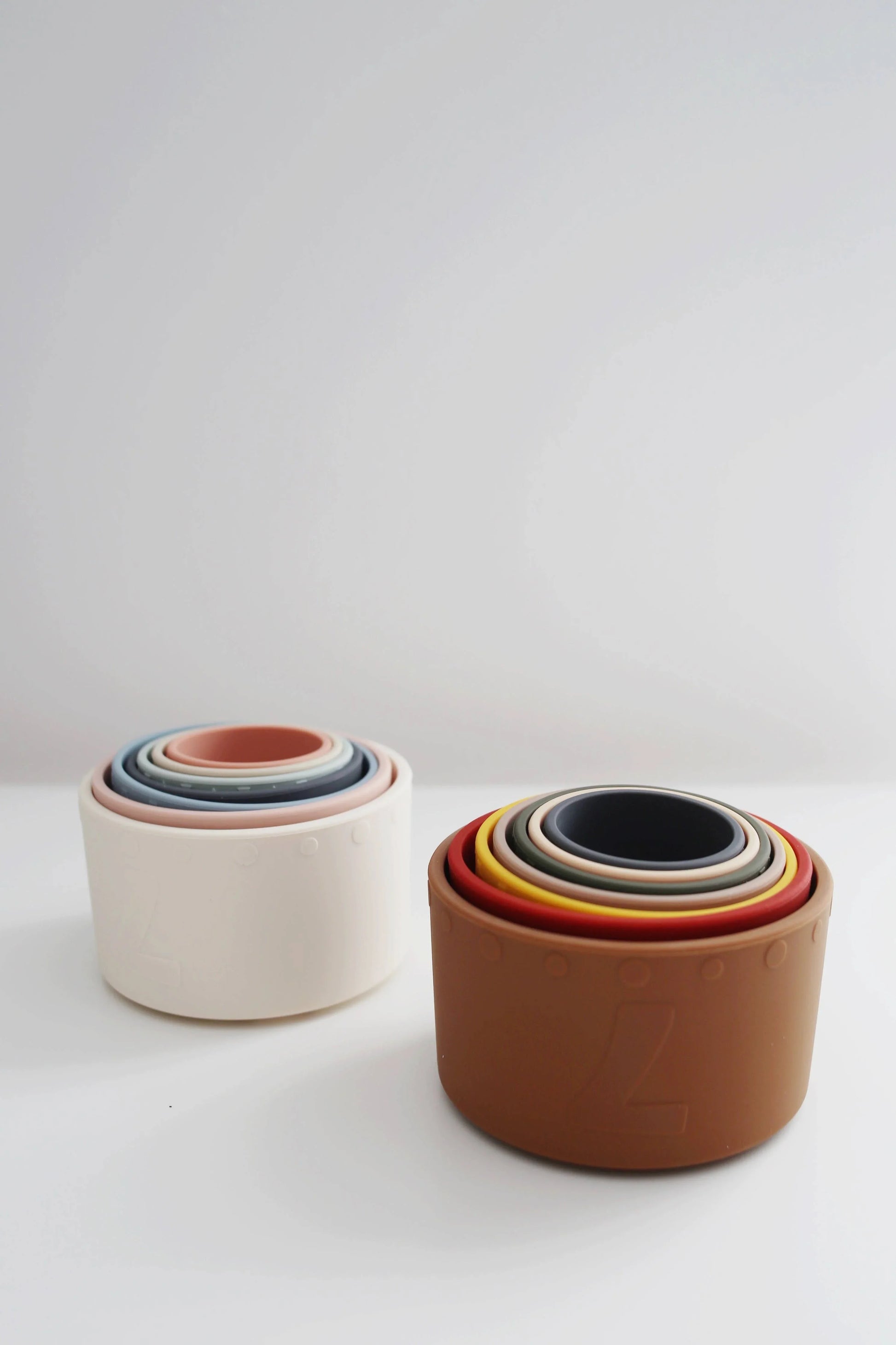Two sets of colorful silicone stacking bowls on a white surface, minimal background. Come see us at Awaken, Franklin, Tennessee