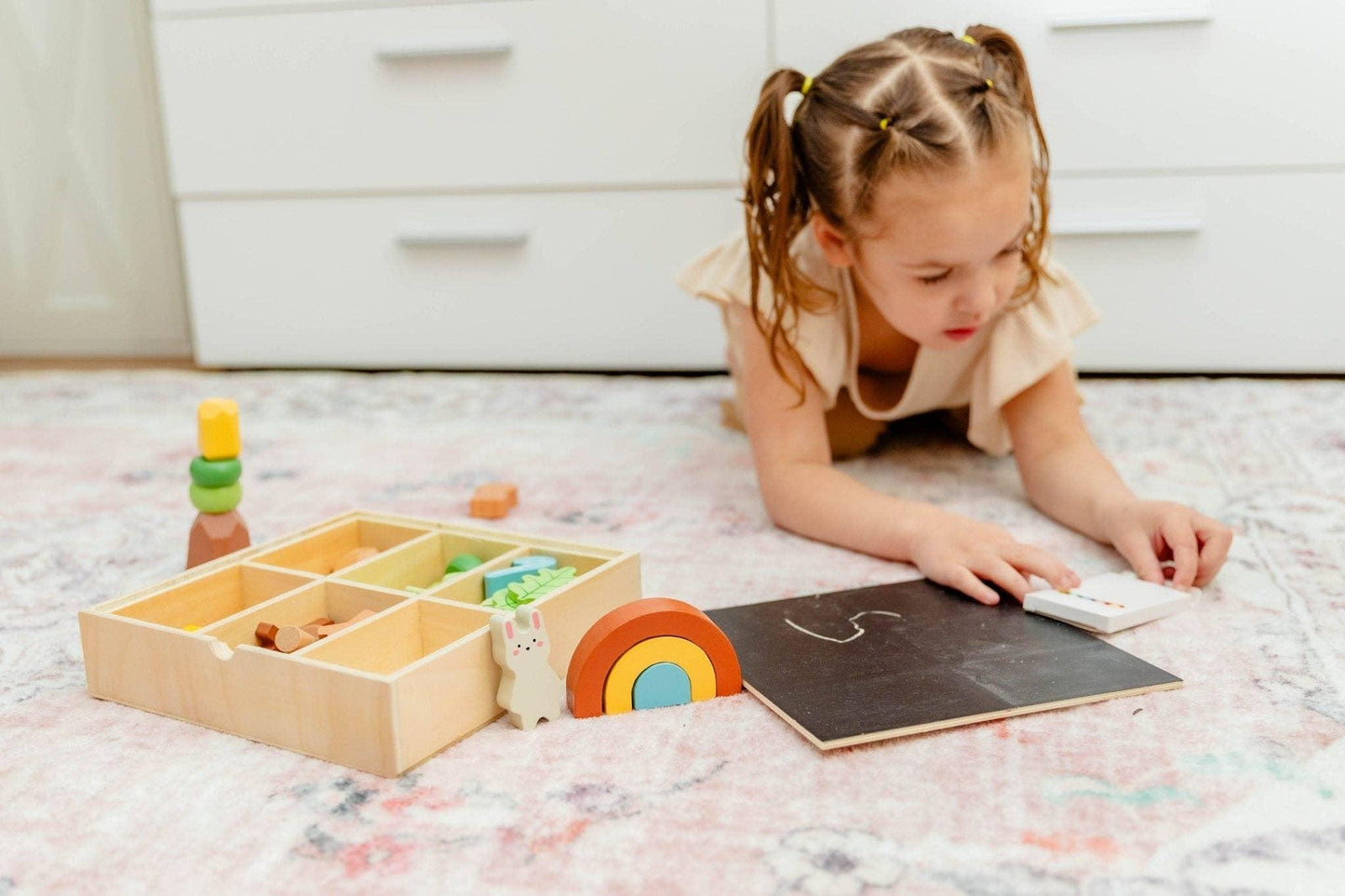 Young girl playing with educational wooden toys and chalkboard on rug at home. Come see us at Awaken, Franklin, Tennessee