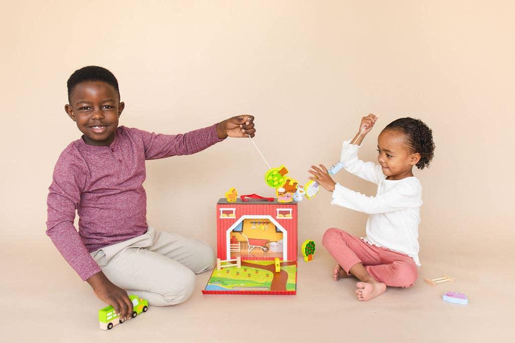 Two children playing with a colorful wooden farm toy set on beige floor. Come see us at Awaken, Franklin, Tennessee