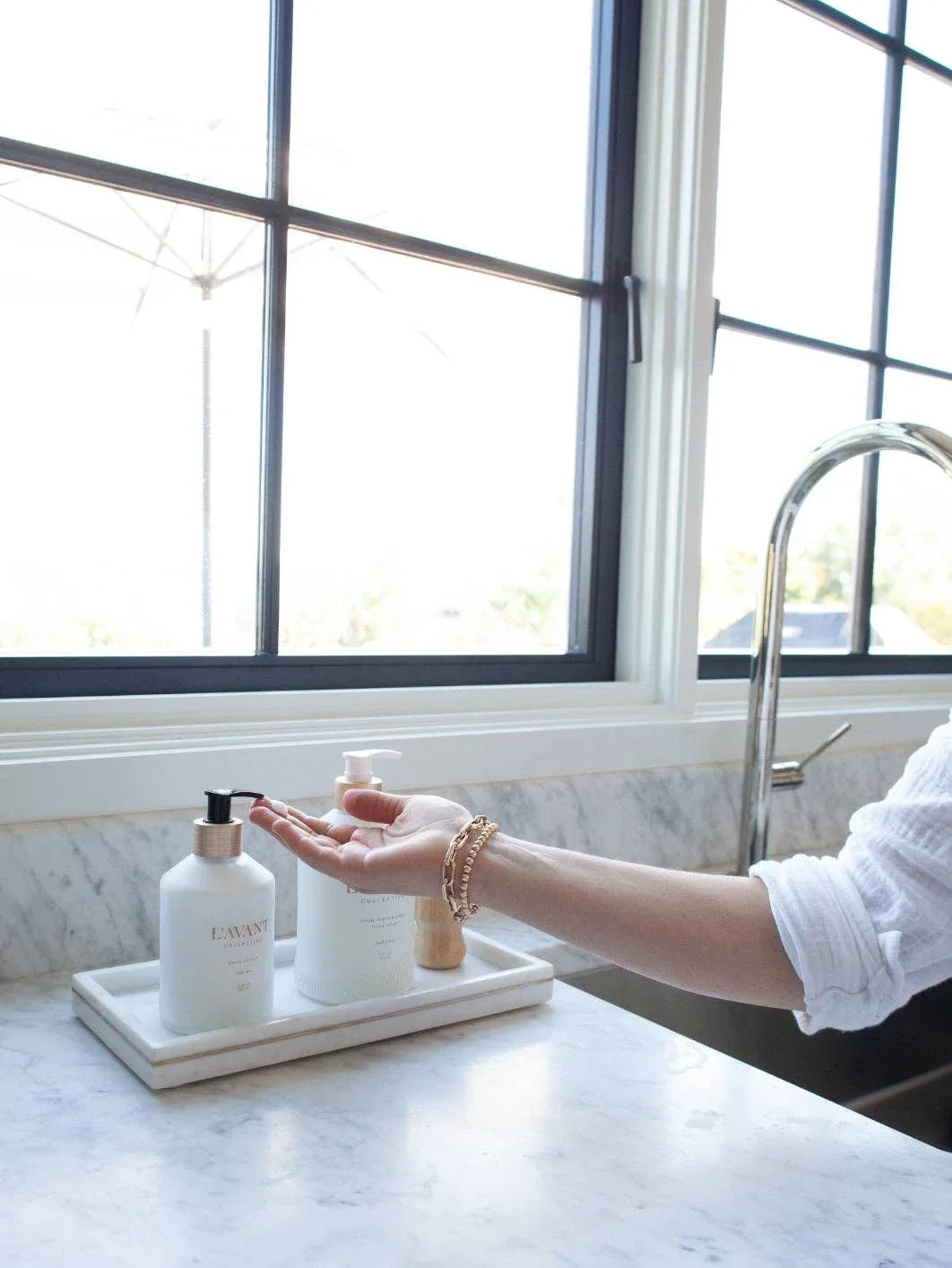 Hand pressing L’AVANT soap dispenser on marble kitchen counter, Come see us at Awaken, Franklin, Tennessee