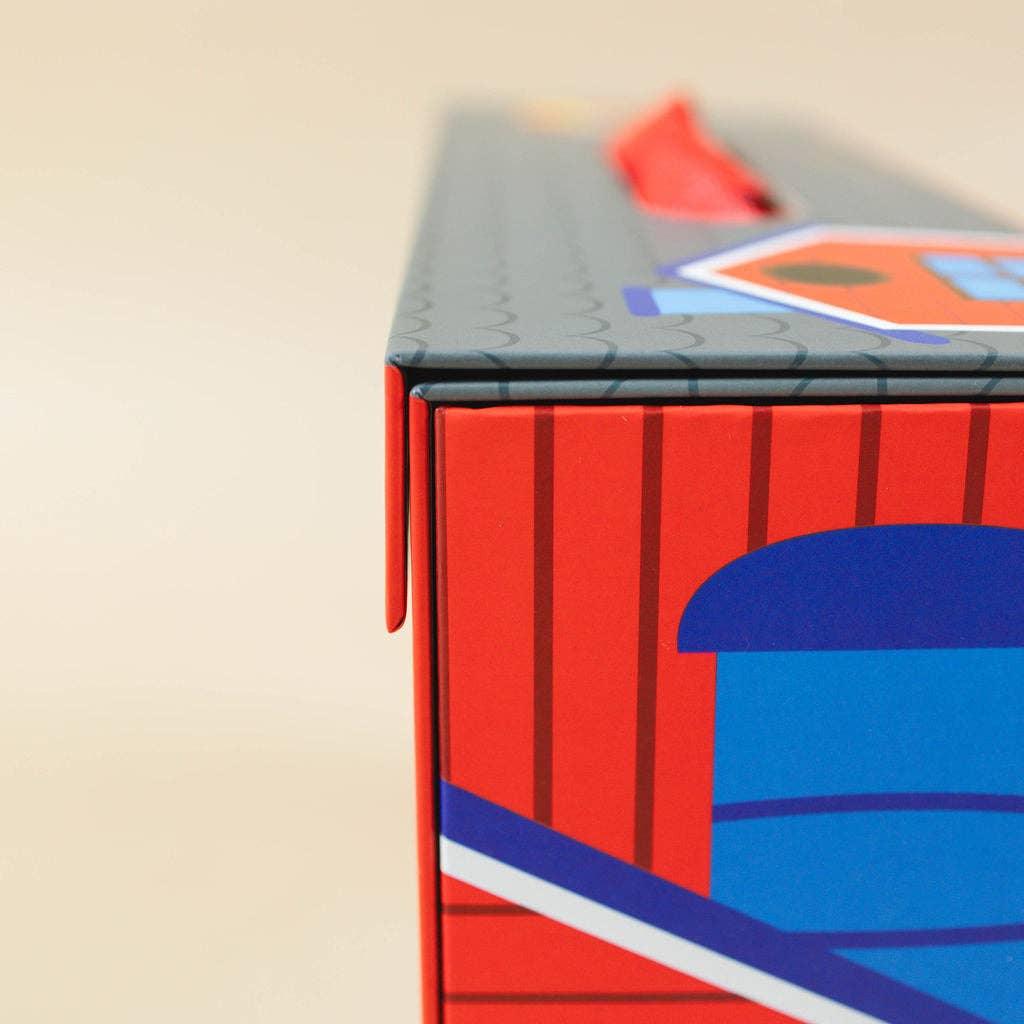 Close-up of colorful red and blue box with house illustration on a beige background. Come see us at Awaken, Franklin, Tennessee