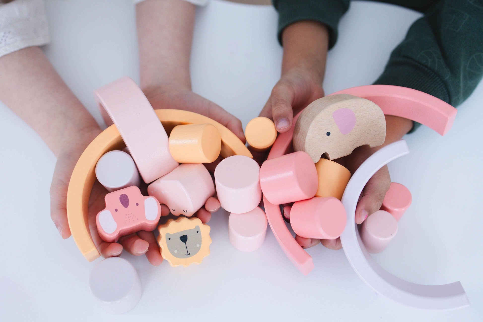 Children holding pastel wooden animal and geometric toys on white table. Come see us at Awaken, Franklin, Tennessee