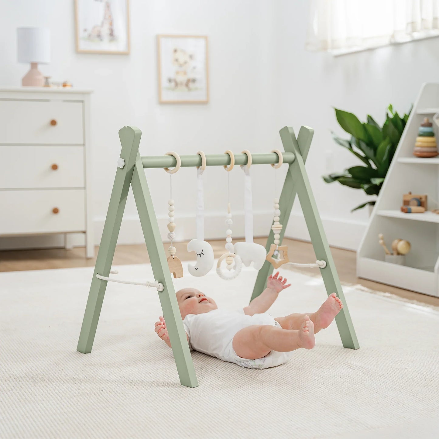 Baby playing on green wooden gym with hanging plush toys in bright nursery, Come see us at Awaken, Franklin, Tennessee