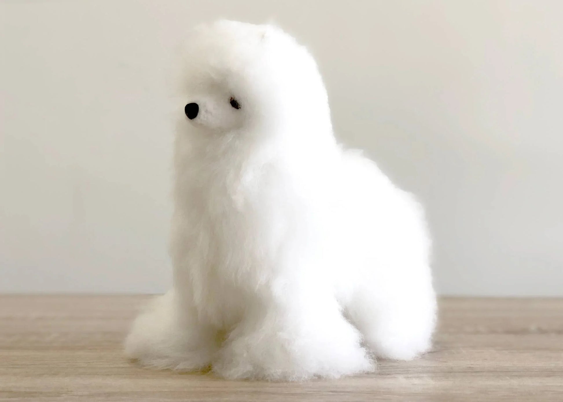 White fluffy dog figurine on wood surface with neutral background. Come see us at Awaken, Franklin, Tennessee