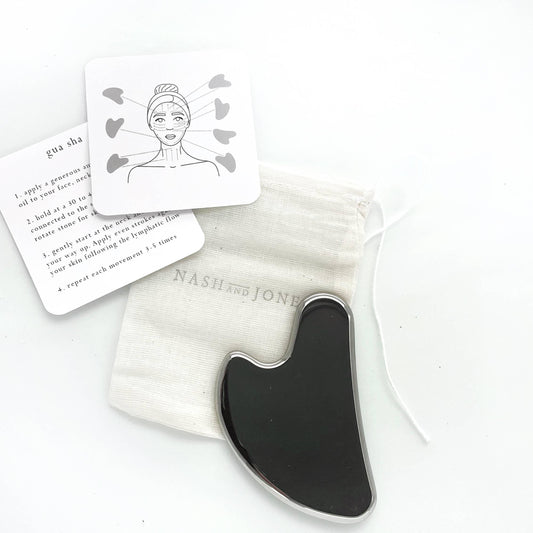 Black gua sha tool with instruction cards and pouch on white background. Come see us at Awaken, Franklin, Tennessee