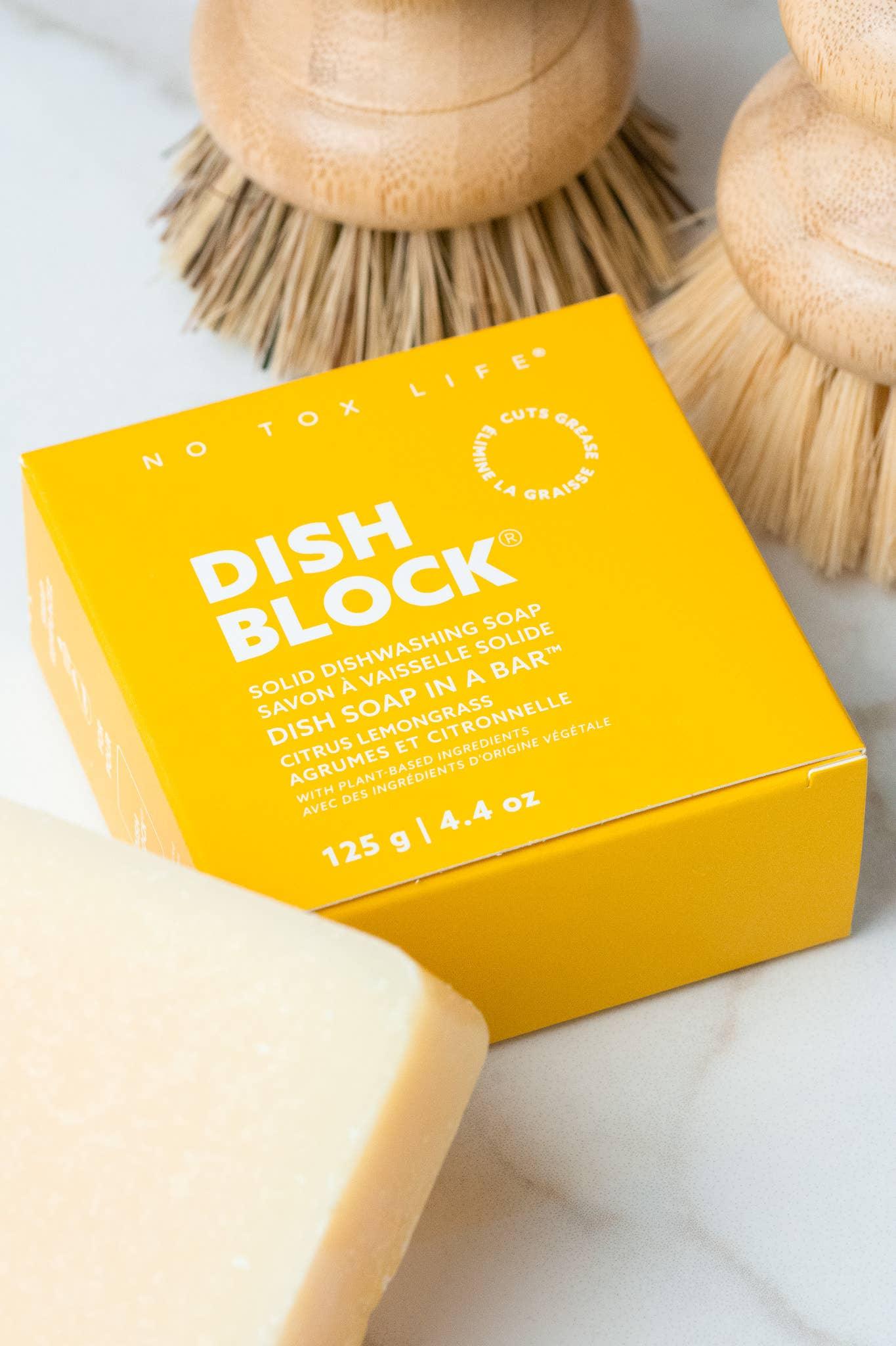 Yellow box of Dish Block solid dishwashing soap with wooden dish brushes on marble surface. Come see us at Awaken, Franklin, Tennessee