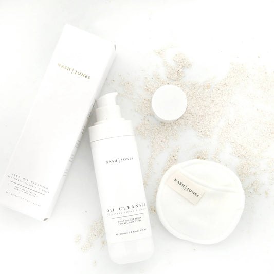 Nash | Jones oil cleanser with packaging and facial pad on white surface with powder scattered. Come see us at Awaken, Franklin, Tennessee