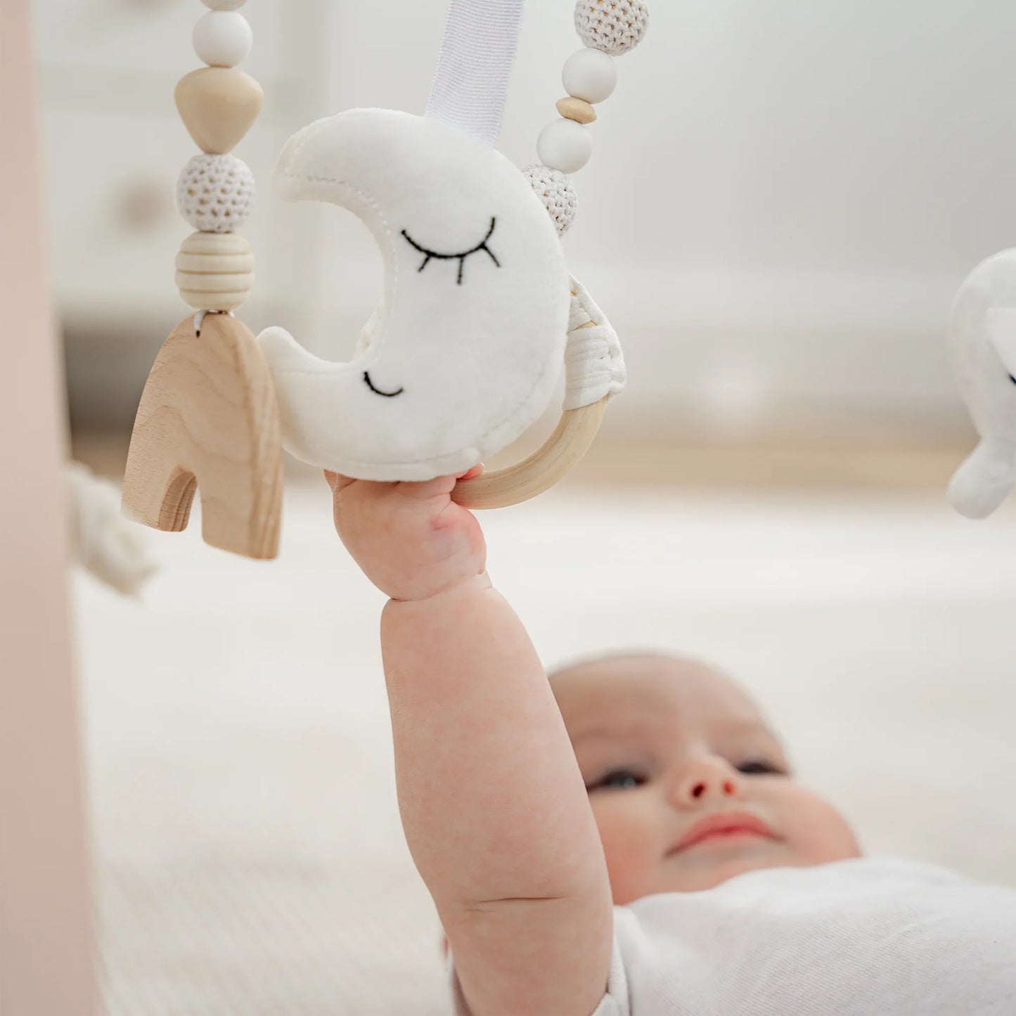 Baby lying on back reaching for soft moon and wooden toys on play gym. Come see us at Awaken, Franklin, Tennessee