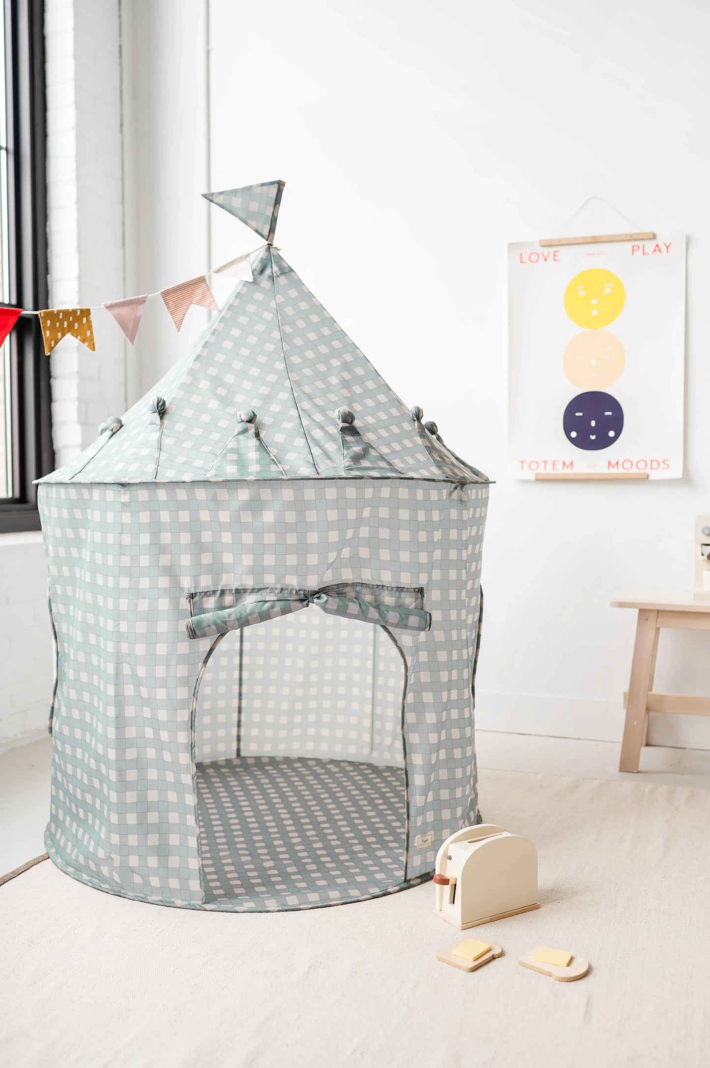 Checkered fabric play tent with colorful bunting and wooden toy toaster in bright kids room. Come see us at Awaken, Franklin, Tennessee
