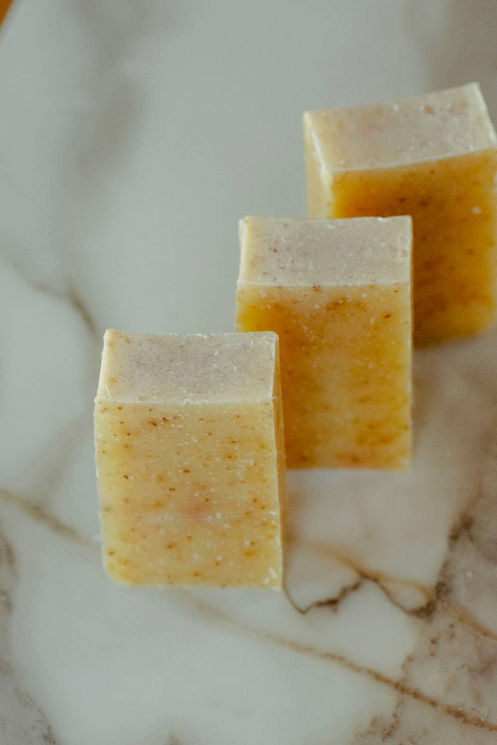Three square bars of natural exfoliating soap on a marble surface. Come see us at Awaken, Franklin, Tennessee