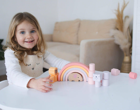 Smiling girl playing with pastel wooden stacking toys at white table in cozy room. Come see us at Awaken, Franklin, Tennessee