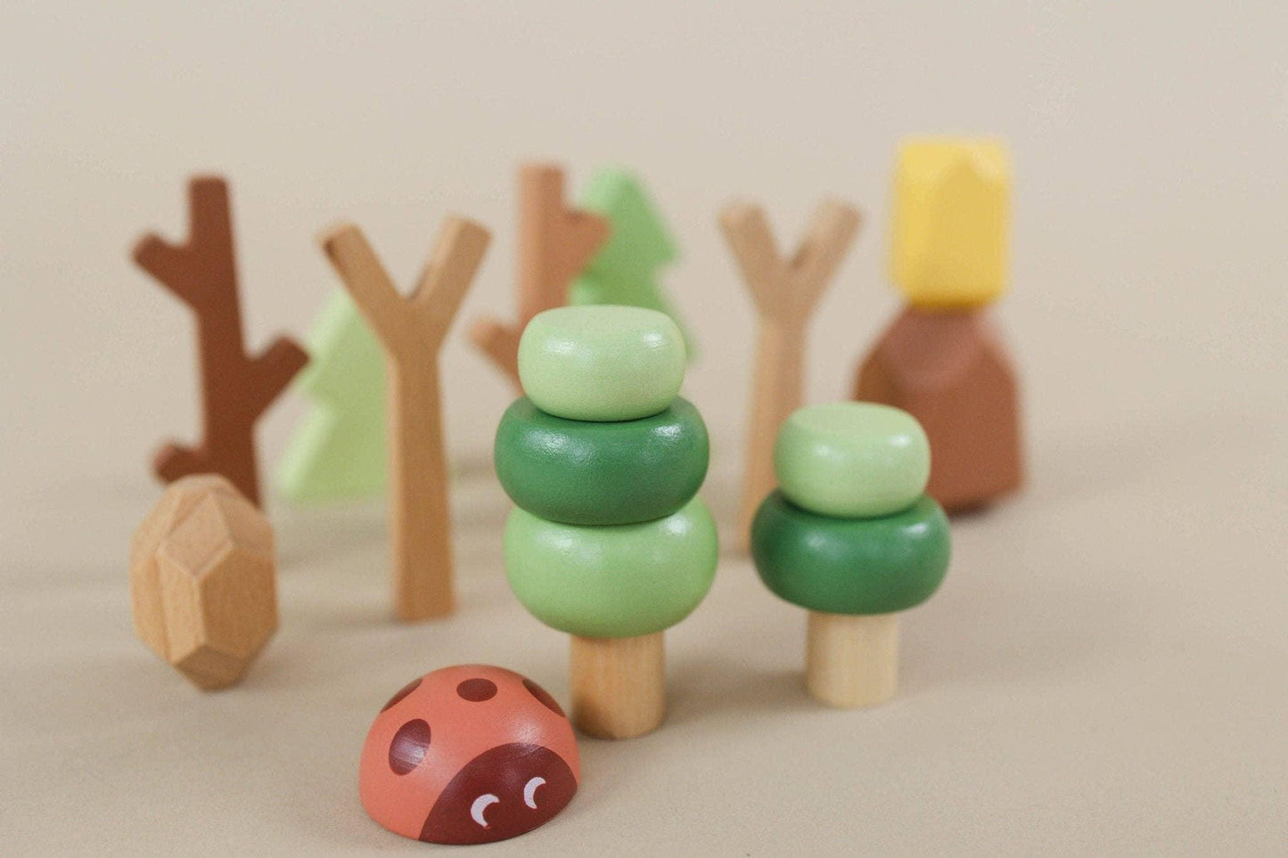 Wooden toy forest set with trees and a ladybug on beige background. Come see us at Awaken, Franklin, Tennessee