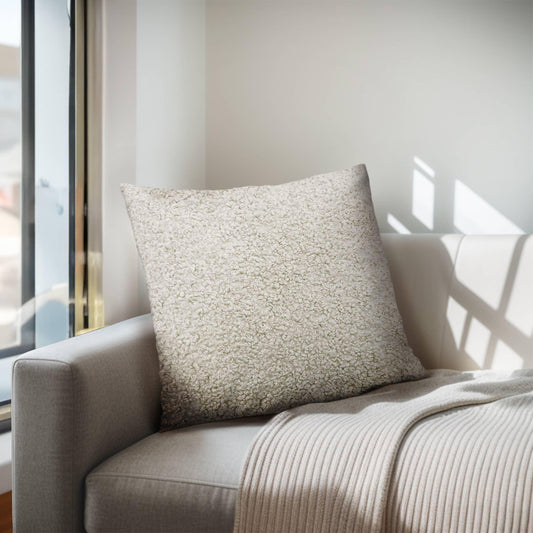 Cozy beige sherpa pillow on light gray sofa with knitted throw near window, bright sunlight. Come see us at Awaken, Franklin, Tennessee