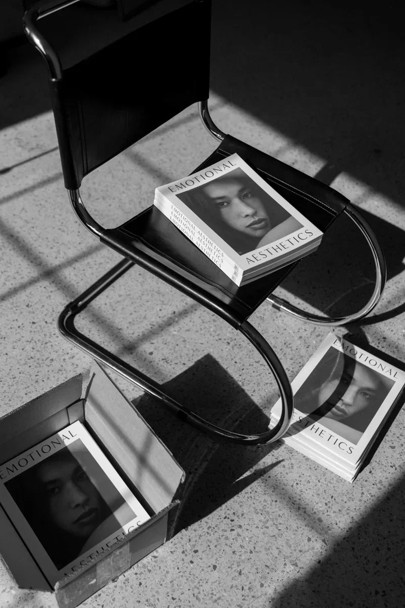 Black chair with books titled Emotional Aesthetics on it and beside box on floor in sunlight, Come see us at Awaken, Franklin, Tennessee
